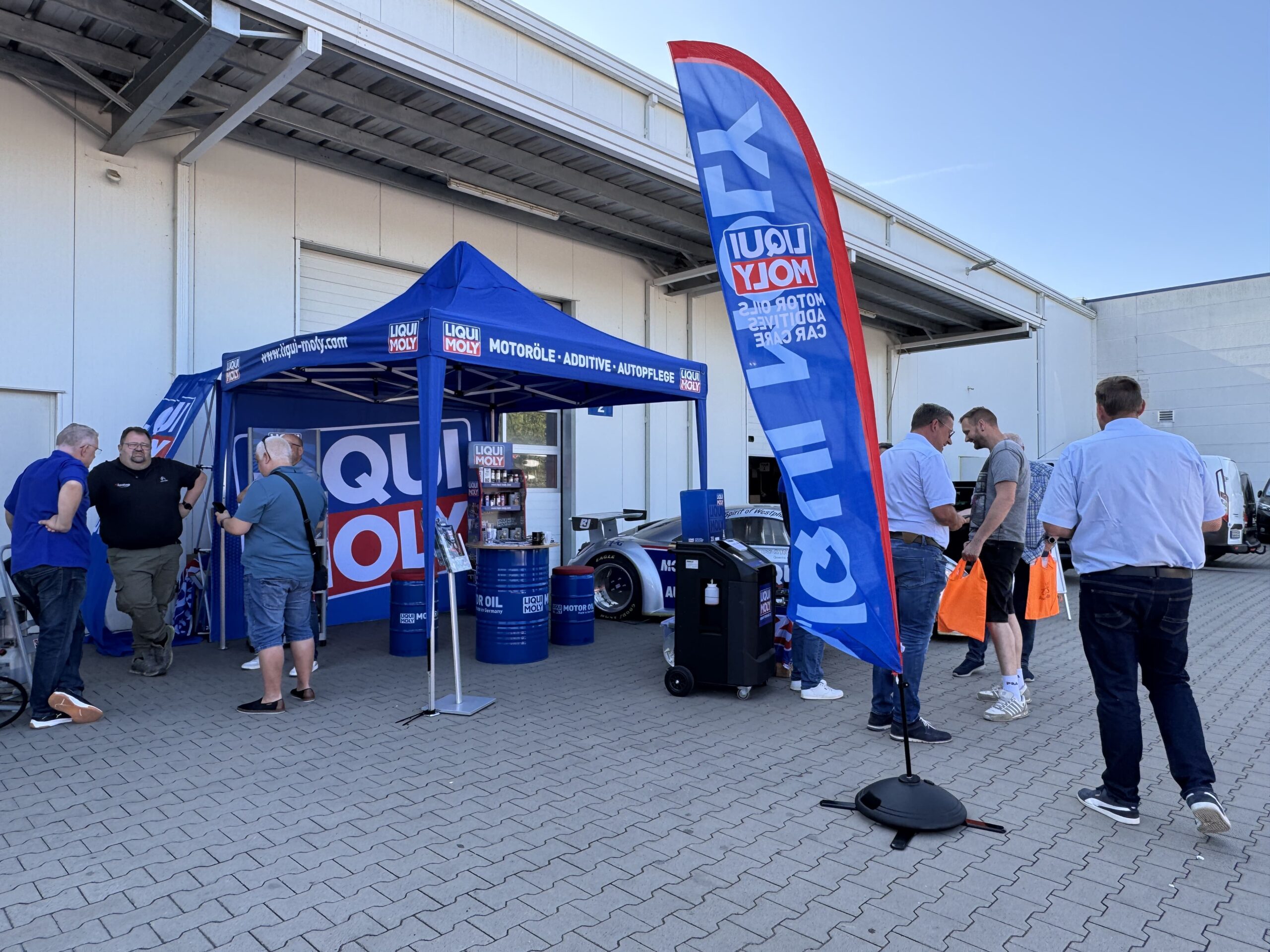 Messestand von LIQUI MOLY im Außenbereich mit blauer Pavillonüberdachung, Werbeflagge und mehreren Besuchern im Gespräch
